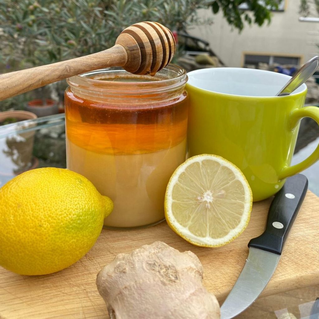 Ein Glas Honig, eine aufgeschnittene Zitrone, ein Stück Ingwer und eine Tasse Tee
