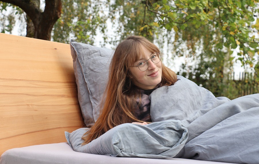 Eine junge Frau liegt in einem Biobett in der Natur und lächelt in die Kamera