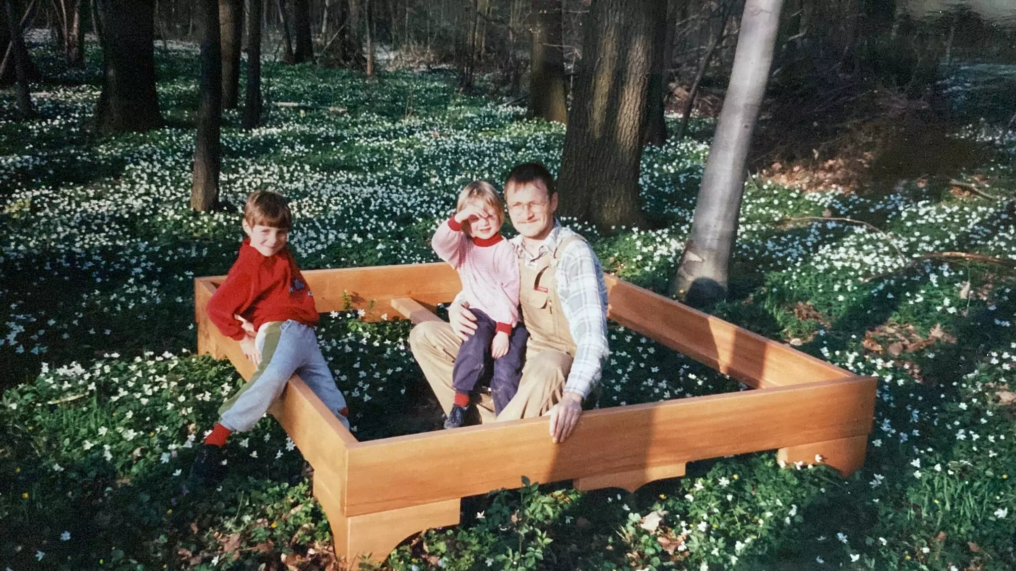 Biobett Erfinder Peter Grube sitzt mit 2 Kindern im Bettrahmen eines Biobetts im Wald