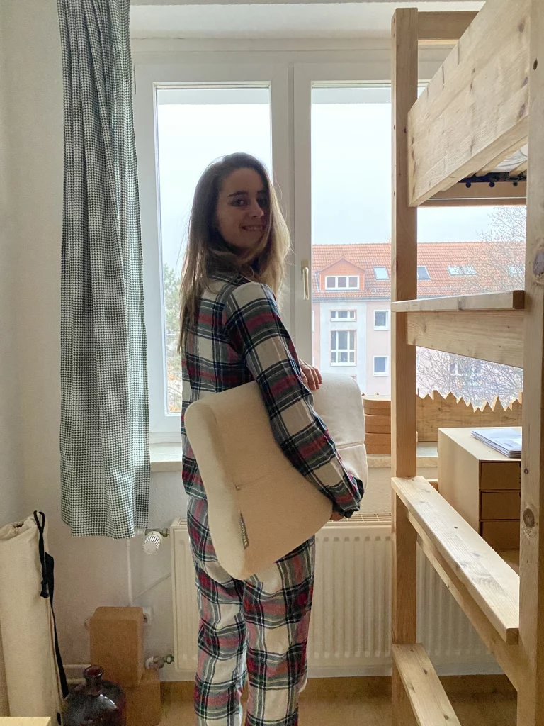 Biobett Kundin Maxi steht mit einem Nackenstützkissen unter dem Arm in ihrem Zimmer