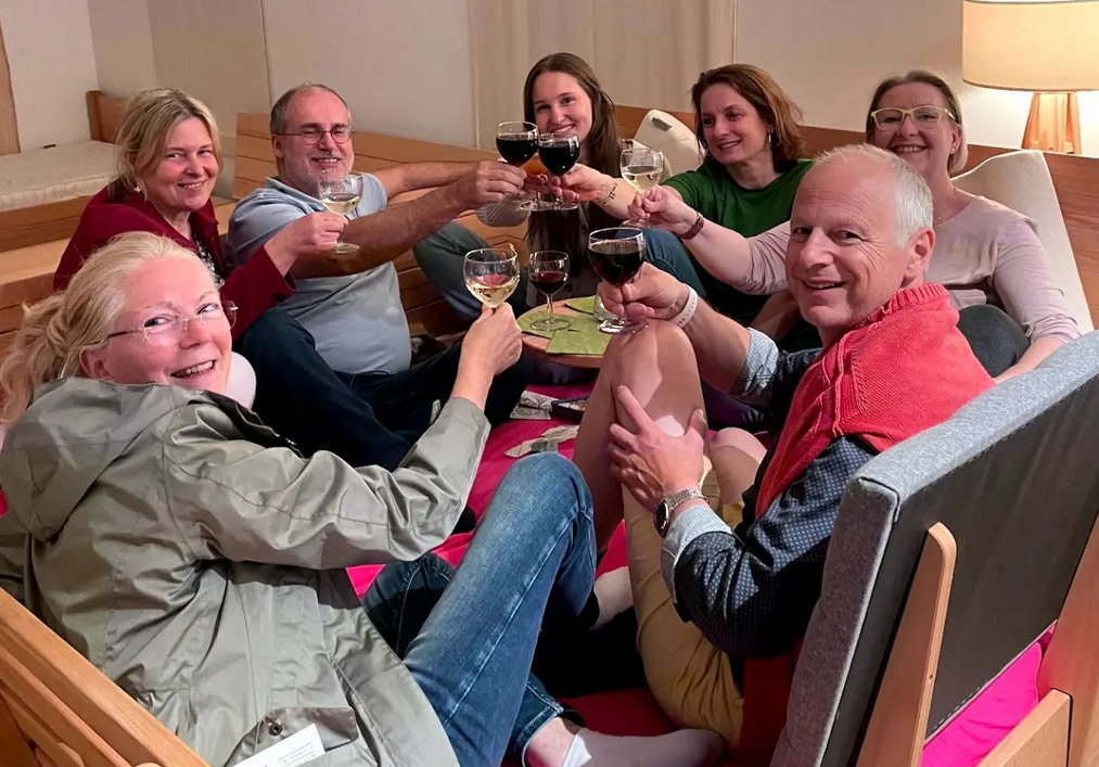 Viele Gäste sitzen bei Wein im Bett Erfurt im Doppelbett um einen Tisch und prosten sich gegenseitig zu