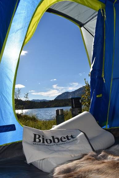 Ein Ausblick aus einem Zelt mit einem Biobett Nackenstützkissen im Vordergrund und einem See im Hintergrund